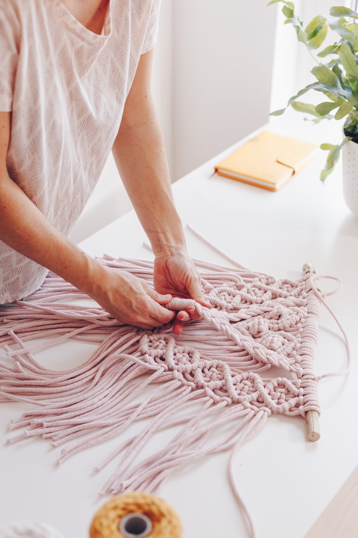 Close up of female hands weaving macrame in a home workshop.